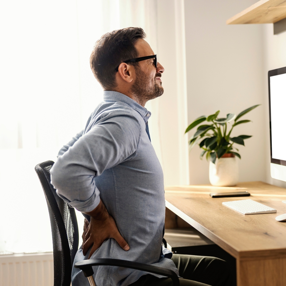 Person sitting on a chair, holding lower back in discomfort, seeking non-surgical back pain relief in Chicago with regenerative treatments.